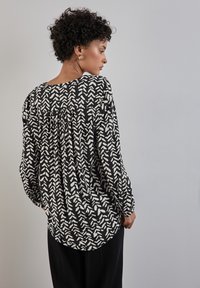Blusa nera con motivo astratto bianco, tessuto leggero, vestibilità ampia, scollatura rotonda, dettaglio arricciato sul retro, maniche lunghe.