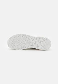 Semelle de chaussure de sport blanche avec un motif en caoutchouc texturé et une bande de roulement visible. Bords légèrement courbés, conçus pour la stabilité et l'adhérence.