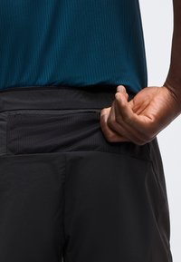 Χέρι τραβάει φερμουάρ σε μαύρη πίσω τσέπη σκούρου παντελονιού, φορά υφασμάτινο σκούρο μπλε πουκάμισο, κοντινό πλάνο στη μέση και το χέρι.