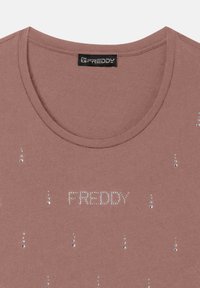 Camiseta de manga corta color rosa polvo, con cuello redondo, que presenta strass y el nombre de la marca "FREDDY" en el centro, de textura suave de algodón.