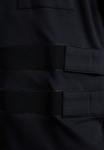 Tessuto nero con due strisce orizzontali di velcro nero testurizzato. Include una piccola tasca applicata sopra le cinghie. Finitura liscia e opaca.