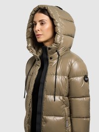 Chaqueta de invierno acolchada color caqui con una gran capucha, que cuenta con una cremallera frontal, cordones ajustables y una parche con logo en el hombro. Textura suave y brillante.