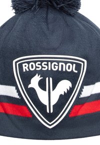 Námořnická pletená čepice s pom-pomem na vrchu, se znakem bílého štítu s designem kohouta a červenobílými horizontálními pruhy.