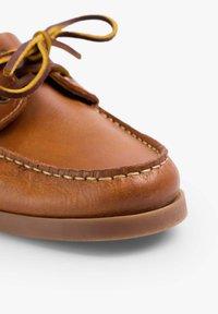 Bruine leren schoen met een ronde neus, contrasterende lichte stiksels en een bruine rubberen zool. Veters in donkerbruin met gele accenten.