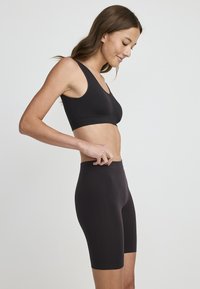 Czarny sportowy stanik i dopasowane, wysokie szorty, wykonane z gładkiego, elastycznego materiału. Stanik ma dekolt w serek bez widocznych szwów.