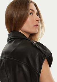 Zwart leren sans-mouwen jas met een brede kraag en een knoopaccent. De textuur is glad, met zichtbare, op maat gemaakte stiksels.