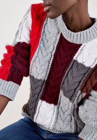 Gruby sweter z dzianiny w blokach czerwonego, szarego, białego i brązowego koloru. Teksturalny wzór w warkocze z prążkowanymi mankietami i dekoltem.