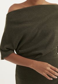 Olivengrünes, geripptes Kleid mit schulterfreiem Design, aus weichem Strickstoff gefertigt. Es zeichnet sich durch eine lockere Passform mit fließenden Ärmeln und einer eng anliegenden Taille aus.