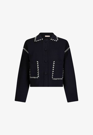 Veste noire à manches longues avec boutons-pression, bordée de coutures blanches sur le col, les poches et les épaules, dotée de deux poches avant.