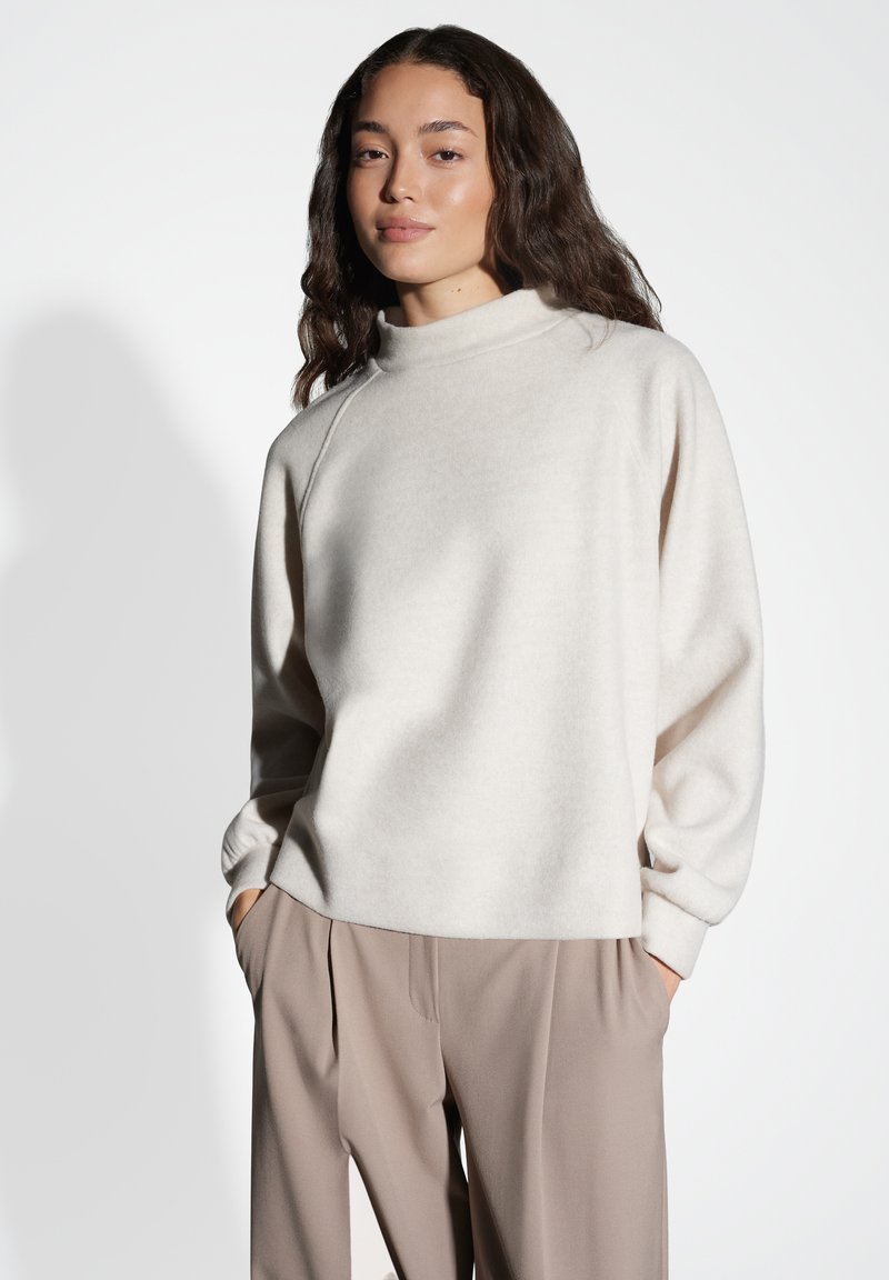Pullover morbido color beige chiaro con collo alto e spalle scese. Polsini aderenti, vestibilità rilassata, abbinato a pantaloni beige.