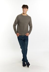 Maglione grigio chiaro a maglia con orlo e polsini a coste, abbinato a jeans blu e sneakers scure, indossato da una figura maschile in piedi.