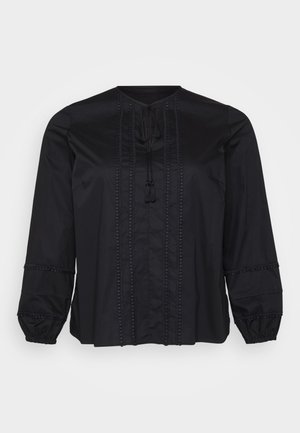 Blusa nera con maniche lunghe, dotata di un colletto rotondo, cuciture decorative e lacci con pon pon. Accenti testurizzati lungo le maniche.