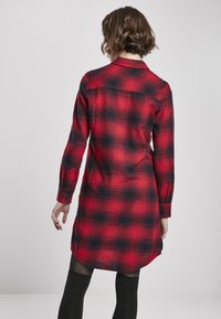 Robe chemise à manches longues à carreaux rouges et noirs, avec un col, des poignets boutonnés et un ourlet incurvé, fabriquée à partir d'un tissu texturé doux.