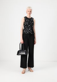 Sort prikket peplum topp med plisserte detaljer, kombinert med vide svarte bukser. Modellen holder en liten svart håndveske og har på seg beige sandaletter med rem.
