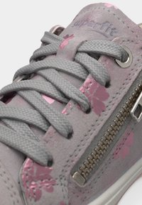Baskets gris clair avec motifs floraux roses, lacets gris et une fermeture éclair latérale argentée, montrant des coutures détaillées et le nom de la marque embossé sur la languette.
