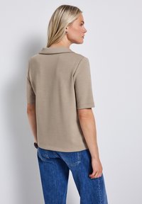 Beige poloshirt met korte mouwen en kraag, gemaakt van een gladde stof, gecombineerd met blauwe denim jeans, met een relaxte pasvorm en een eenvoudig ontwerp.