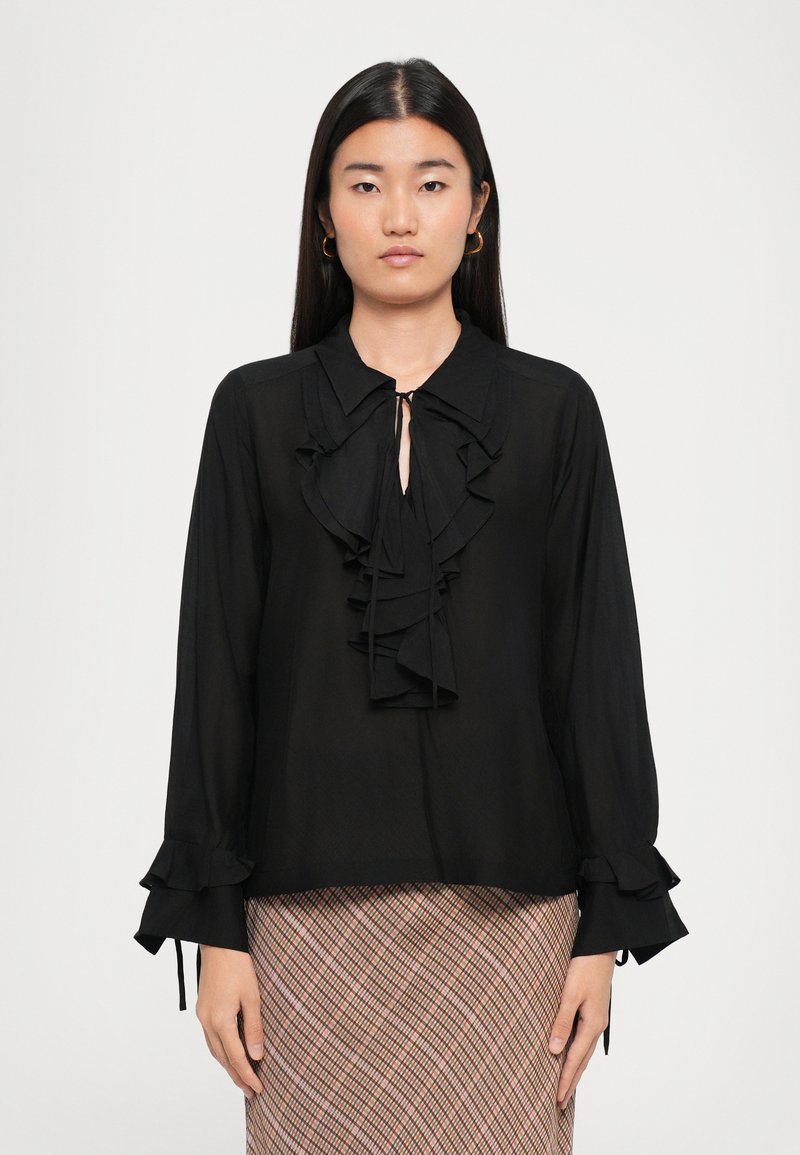 Black blouse with a ruffled front, tie collar, and long sleeves featuring ruffle accents at cuffs. Made from lightweight fabric.