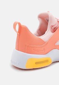 Close-up van de koraalrode en roze Nike Air Max sneakerhak met witte zool en gele luchtkussen detail op een neutrale achtergrond.