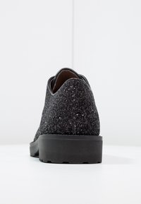 Chaussure noire texturée avec une tige scintillante, une forme arrondie et une semelle extérieure noire unie. Vue arrière mettant en valeur des lignes lisses et une brillance subtile.