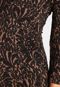 Brun och svart blommönstrad tyg med en texturerad yta, som har volanger längs sömmen och en figurnära form.