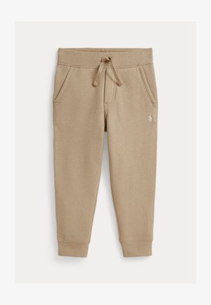 Beżowe spodnie dresowe dla maluchów z elastycznym pasem, sznurkiem, dwiema bocznymi kieszeniami, ściągaczami przy kostkach i małym, białym haftowanym logo na biodrze.