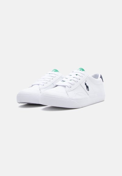 Λευκά αθλητικά παπούτσια χαμηλού ύψους με πράσινη ετικέτα στη γλώσσα, μαύρο λογότυπο στο πλάι, λευκά κορδόνια και λευκές λαστιχένιες σόλες σε απλό φόντο.