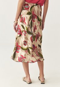 Jupe midi florale en beige, avec des motifs abstraits rouges et verts. Tissu léger et doux avec une silhouette fluide et une fente sur le côté.