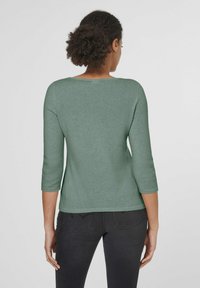 Grüner Pullover mit drei Viertelärmeln, einem runden Ausschnitt und einer weichen Textur. Kombiniert mit schwarzen Jeans, die eine entspannte Passform zeigen.
