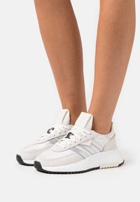 Vita mockasins och mesh-sneakers med en texturerad yta, utrustad med tre horisontella ränder, svarta accenter och en solid gummisula.