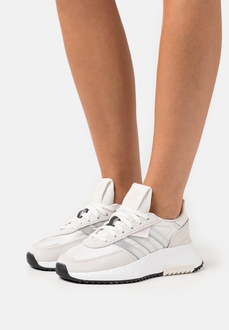 Vita mockasins och mesh-sneakers med en texturerad yta, utrustad med tre horisontella ränder, svarta accenter och en solid gummisula.