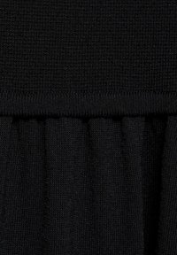 Black textured fabric with a smooth top section and a gathered ruffle below. Material appears knit, emphasizing softness and flexibility.