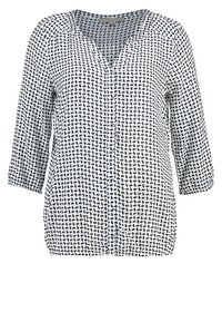 Blouse blanche avec motif à pois noirs irréguliers, col en V, manches 3/4 et ourlet élastique.