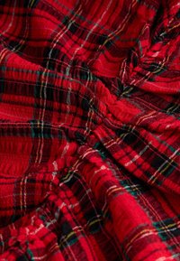 Roter karierten Stoff mit ineinander verwobenen schwarzen, grünen und gelben Fäden. Die Textur ist weich mit gerafften Details in einigen Bereichen.