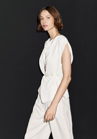 Wit kort mouwtopje met een getailleerde taille en een gedrapeerd ontwerp, gecombineerd met lichtgekleurde, loszittende broek. Eenvoudige, minimalistische esthetiek.