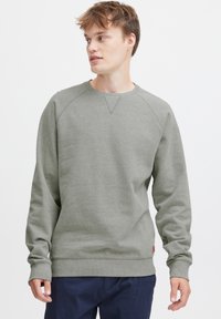 Sudadera gris claro con mangas raglán, cuello y puños de canalé, y una etiqueta de logo discreta en el dobladillo. Tejido suave y texturizado.