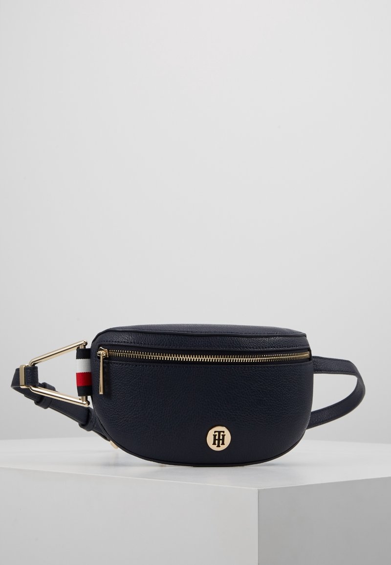 Marsupio in pelle blu navy con zip in tono oro, accentuato dal logo, e tracolla a righe. Forma ovale con finitura testurizzata.