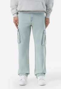 Lysblå cargo bukser lavet af denim, med sidelommer med klap, en løs pasform og kontrastsyninger. Båret med hvide sneakers.