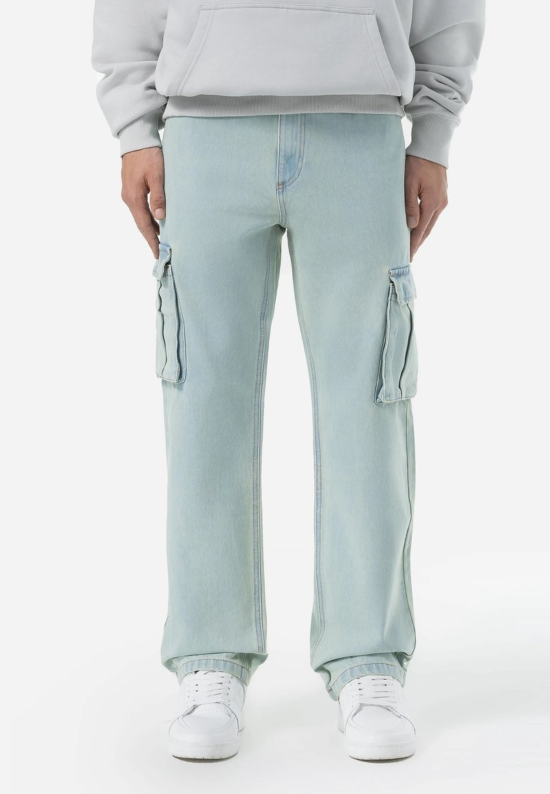 Lysblå cargo bukser lavet af denim, med sidelommer med klap, en løs pasform og kontrastsyninger. Båret med hvide sneakers.