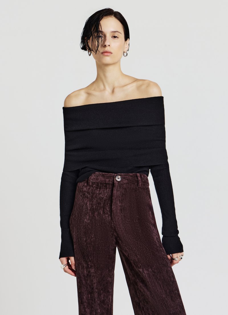 Schwarzes, schulterfreies, geripptes Oberteil kombiniert mit dunklen, strukturierten, bordeauxroten Hosen mit weitem Bein und Knopfverschluss. Sichtbare silberne Ringakzente.