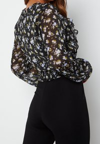 Blusa nera floreale in tessuto leggero e trasparente con collo arricciato e orlo elasticizzato; presenta piccoli motivi di fiori gialli e blu.