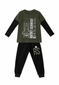 T-shirt verde oliva con design di razzo e testo "SCIENZIATO DEI ROCKET", abbinato a pantaloni jogger neri con ricamo "RS" e stelle.