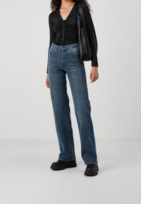 Black long-sleeve top with button closure under a fitted waist, paired with light blue wide-leg jeans and chunky black platform boots.