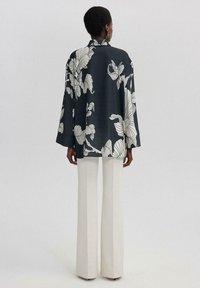 Kimono à manches longues en tissu bleu marine avec de grands motifs floraux blancs. Coupe ample, col mandarin et manches larges. Associé à un pantalon large crème.