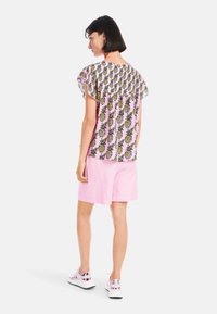 Rosa kurzes Oberteil mit Ananasdruck, kombiniert mit hellrosa Shorts und glänzenden Sneakers, von hinten betrachtet.