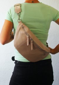 Beige leren schoudertas met twee ritsvakken, verstelbare strap van gemusterde stof en afgeronde vorm voor ergonomisch dragen.