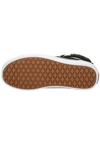 Suela de zapatilla con una superficie texturizada negra, un patrón de tracción de goma marrón y detalles en el borde blancos. Patrón de agarre hexagonal visible.