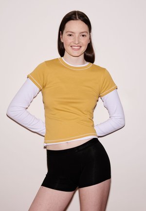 Short-sleeve yellow t-shirt layered over a white long-sleeve shirt, paired with black shorts. The fabric is smooth with contrasting stitching.