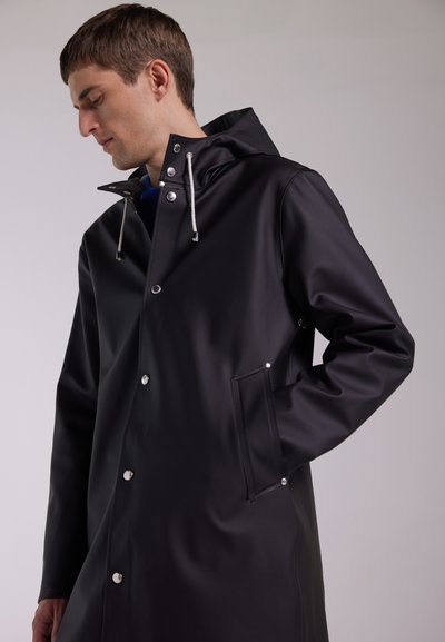 Svart vattentät regnrock av slätt material, med dragkedja vid kragen, silvriga knappar och sidorfickor för funktionalitet.