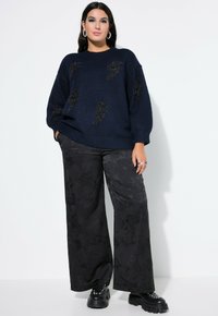 Granatowy sweter z dzianiny z teksturowanymi detalami w kształcie błyskawicy, połączony z czarnymi spodniami wide-leg o wysokim stanie i subtelnym kwiatowym wzorze. Czarne buty na platformie.