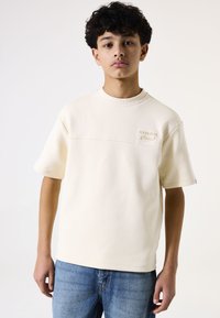 Korte mouwen beige sweater met een ronde hals, voorzien van een textuur logo patch op de borst en een gladde stofafwerking.